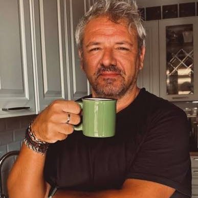 Luca in cucina, maglietta nera, una tazza di caffè verde in mano